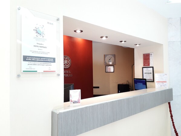 Een hotel receptie met een rode muur, een klok en verschillende ingelijste certificaten.