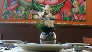 A dining table with a vase of white flowers, a colorful abstract painting on the wall, and a wooden chair.