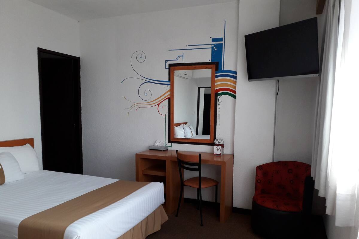 A hotel room with a bed, a desk, a chair, a television, and a mirror.
