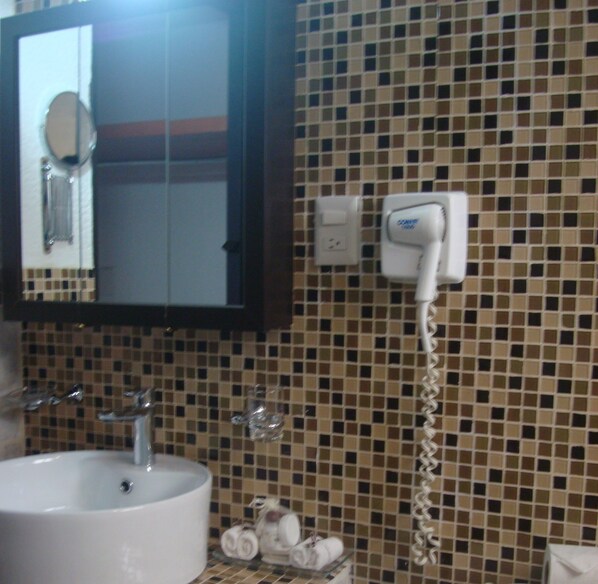 A bathroom with a sink, mirror, and a hairdryer mounted on the wall.
