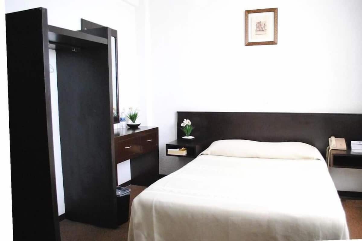 A hotel room with a bed, a dresser, a nightstand, and a framed picture on the wall.