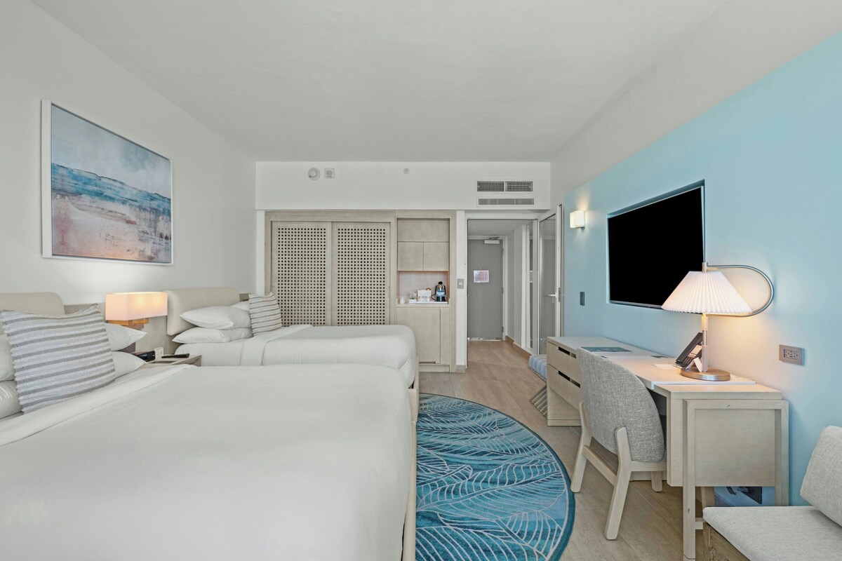 A hotel room with a bed, a desk, a chair, a TV, and a bathroom with a shower and toilet.