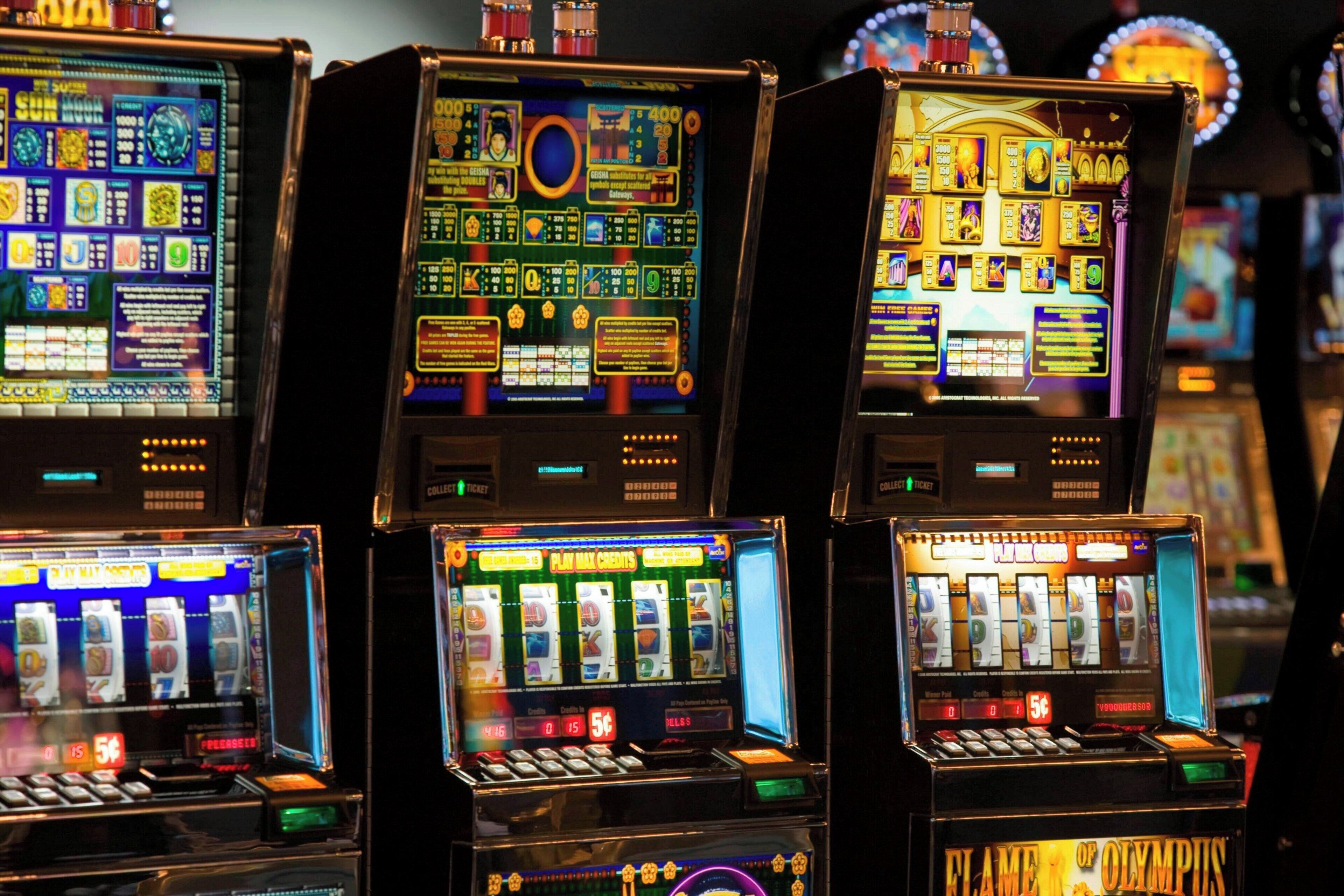A row of slot machines with various game screens and coin payout displays.