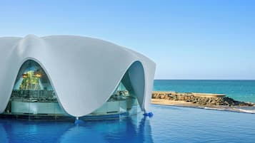 Un edificio moderno con un diseño de techo curvo único, ubicado junto a una piscina con vista al océano.