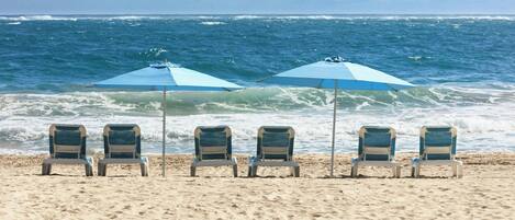 A beach with four chairs and two umbrellas.