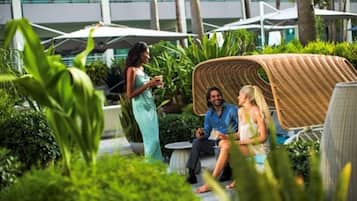 A group of people sitting on outdoor furniture in a lush garden area with a modern building in the background.