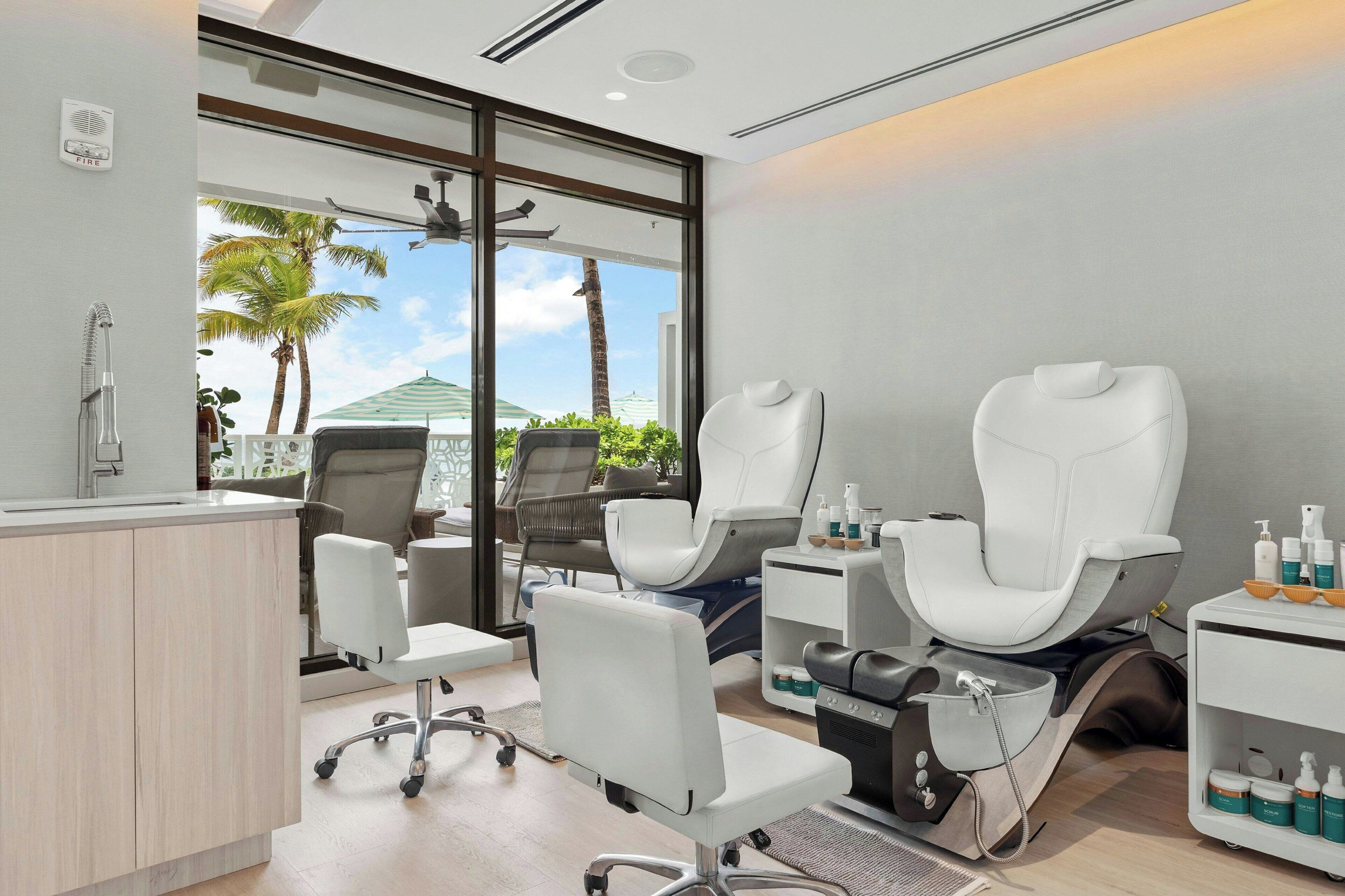 A modern spa room with massage chairs, a reception desk, and a view of palm trees.