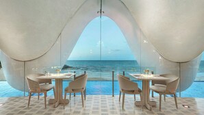 Un espace repas offrant une vue sur la mer, avec des tables et des chaises disposées sous un grand plafond en arc de cercle.