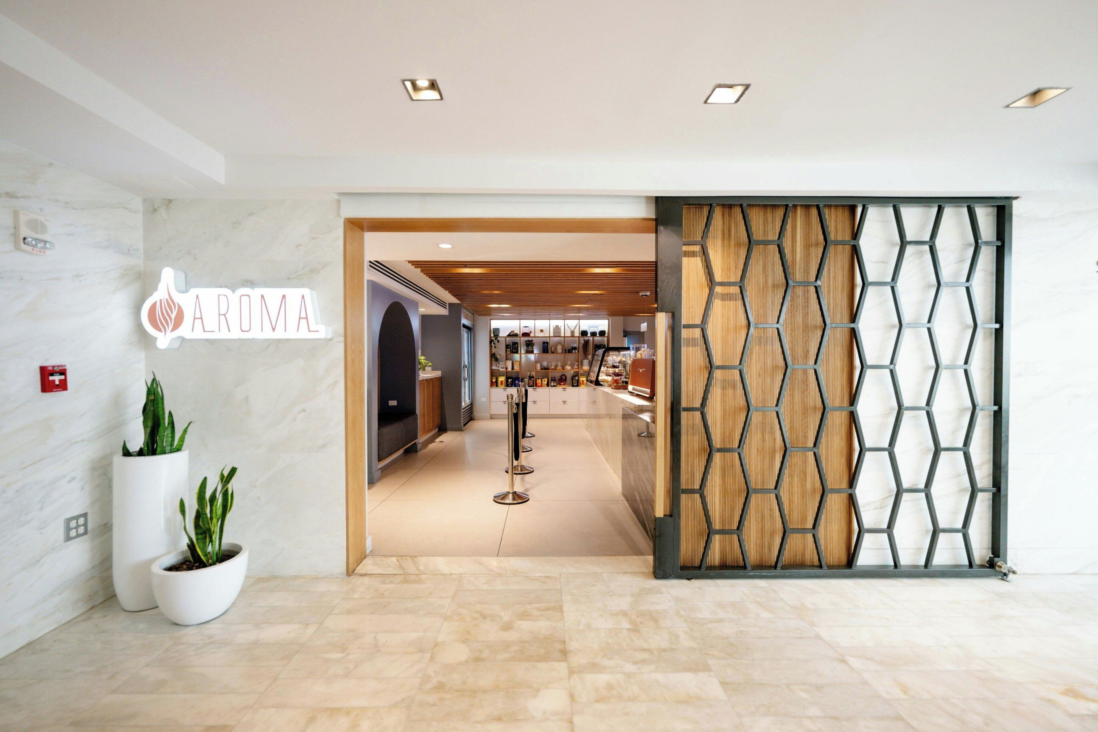 A hotel entrance with a sign reading 'AROMA,' potted plants, a reception desk, and a modern interior design.