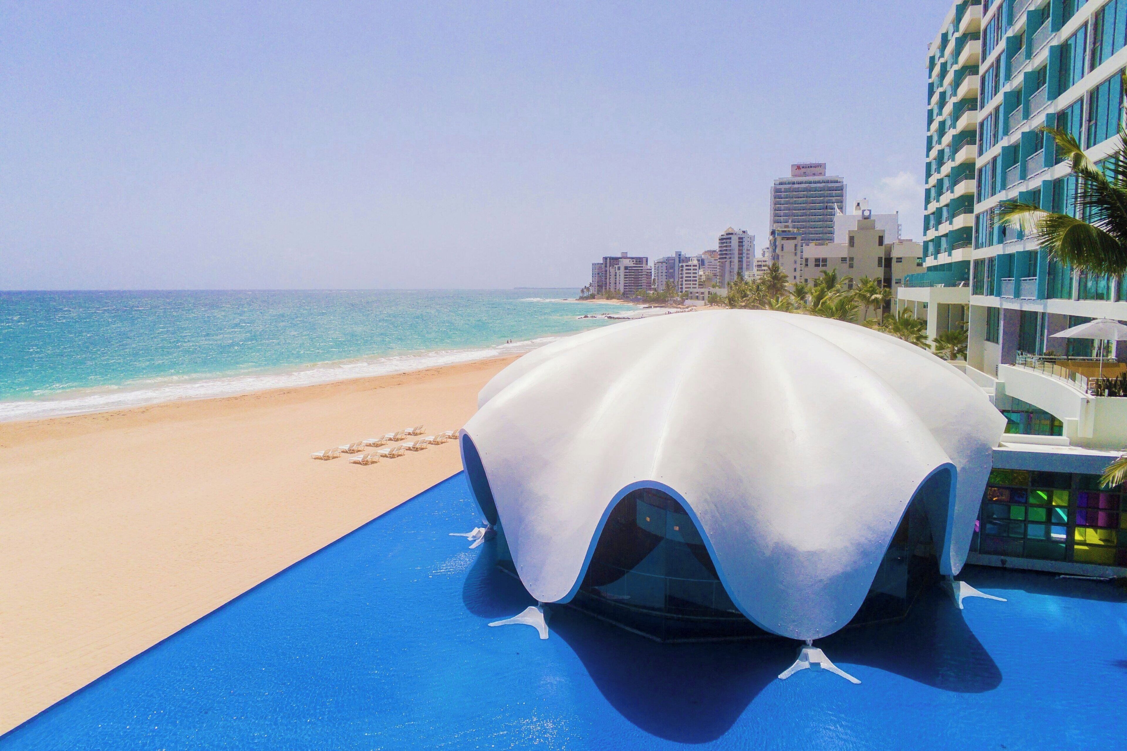 Um hotel moderno com uma estrutura em forma de cúpula única na praia, área de piscina e vista para o oceano e o horizonte da cidade.
