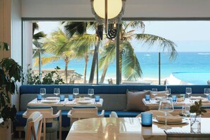 A dining area with tables set for two, blue cushioned seating, and a view of the ocean and palm trees. - La Concha Resort, Puerto Rico, Autograph Collection (San Juan)
