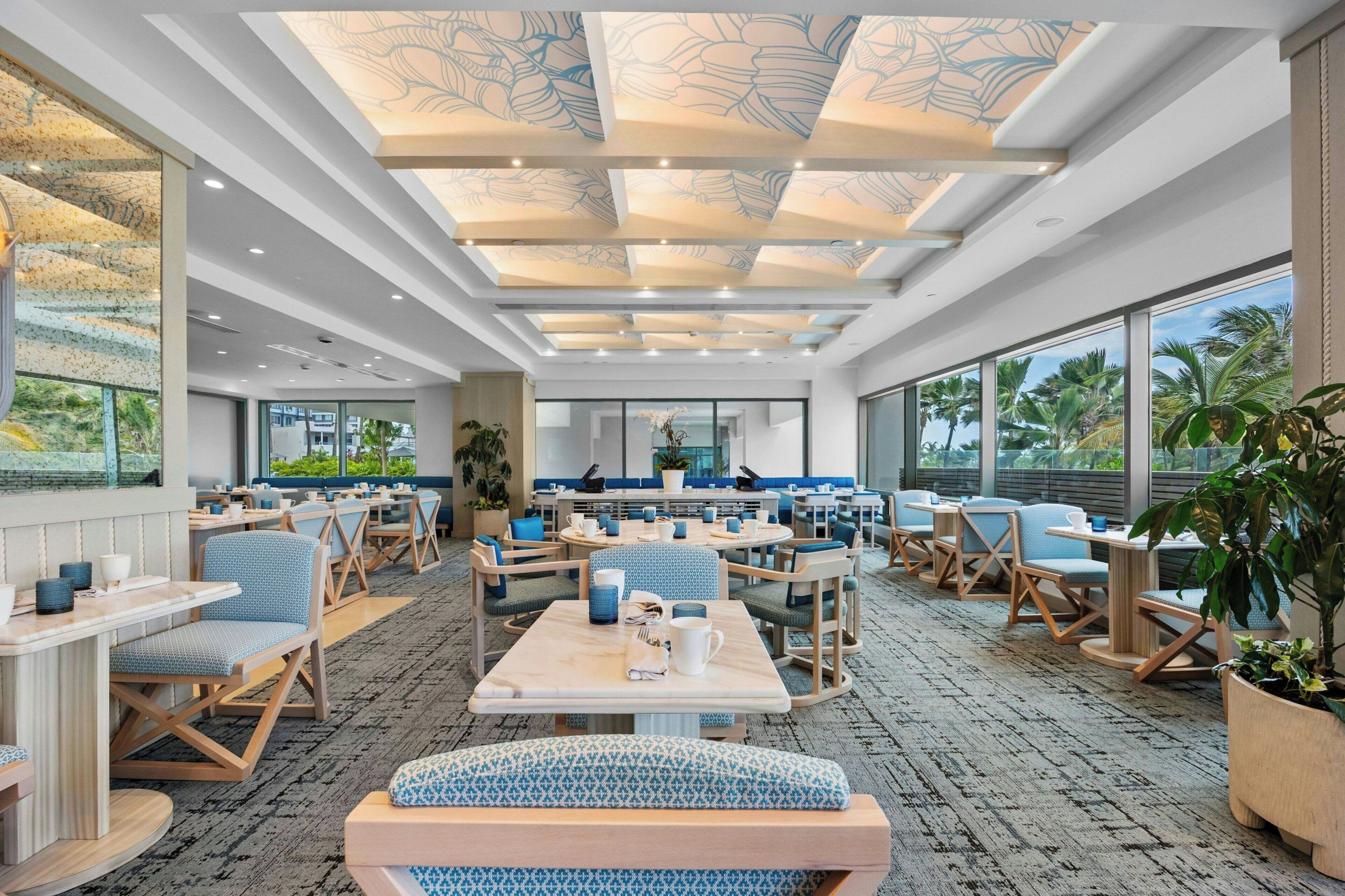 A spacious indoor area with multiple seating arrangements, large windows, and a patterned ceiling.