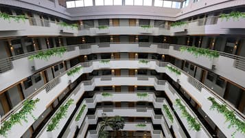 Un atrio de varios niveles con un jardín central, balcones con vegetación y un techo de cristal.