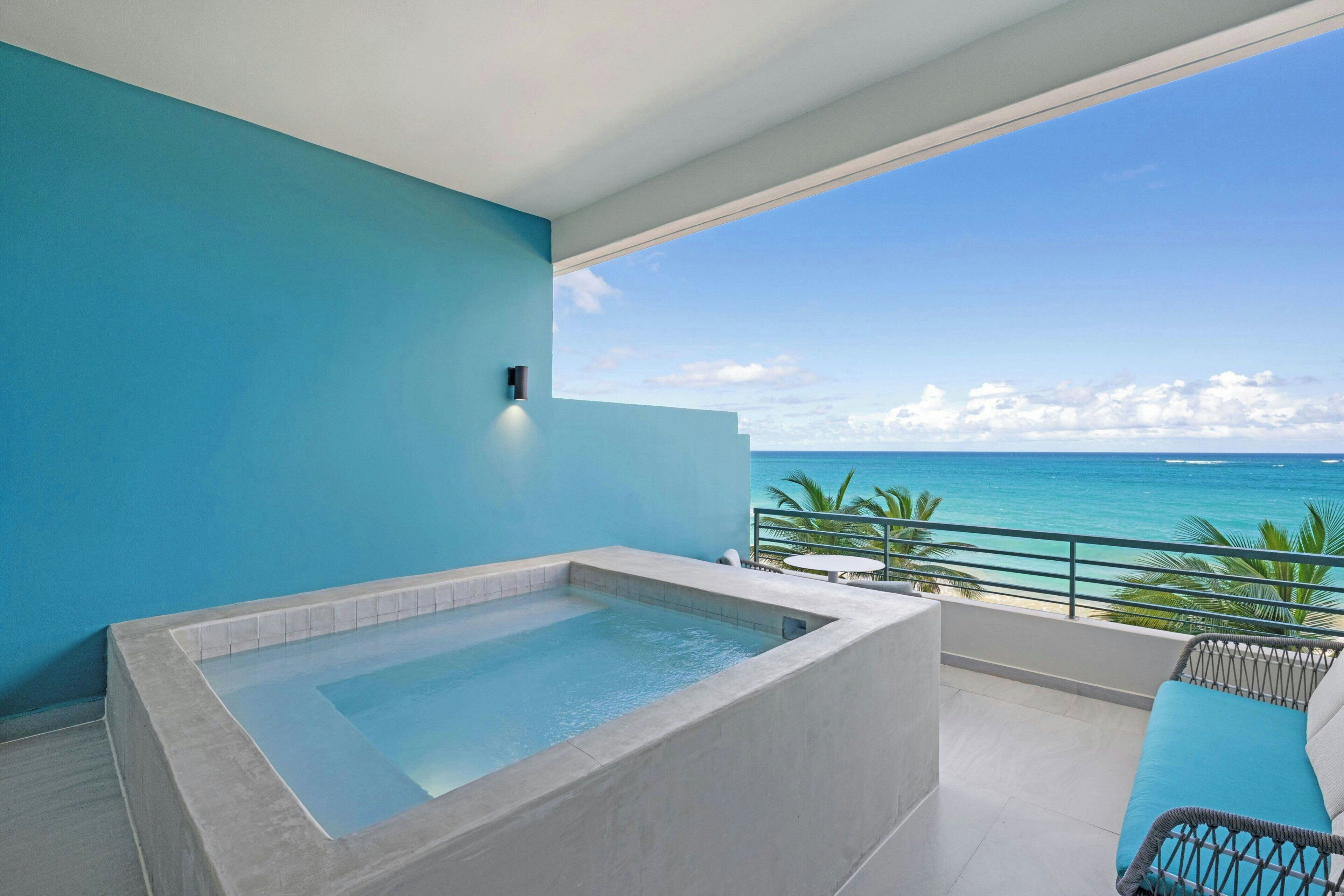 Un balcón moderno con una bañera grande, vista al océano y una pared azul.