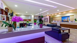 Un moderno vestíbulo de hotel con una recepción, zona de estar y plantas en macetas.