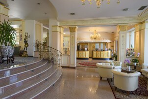 Un lobby espacioso con una escalera de mármol, muebles elegantes y un candelabro.