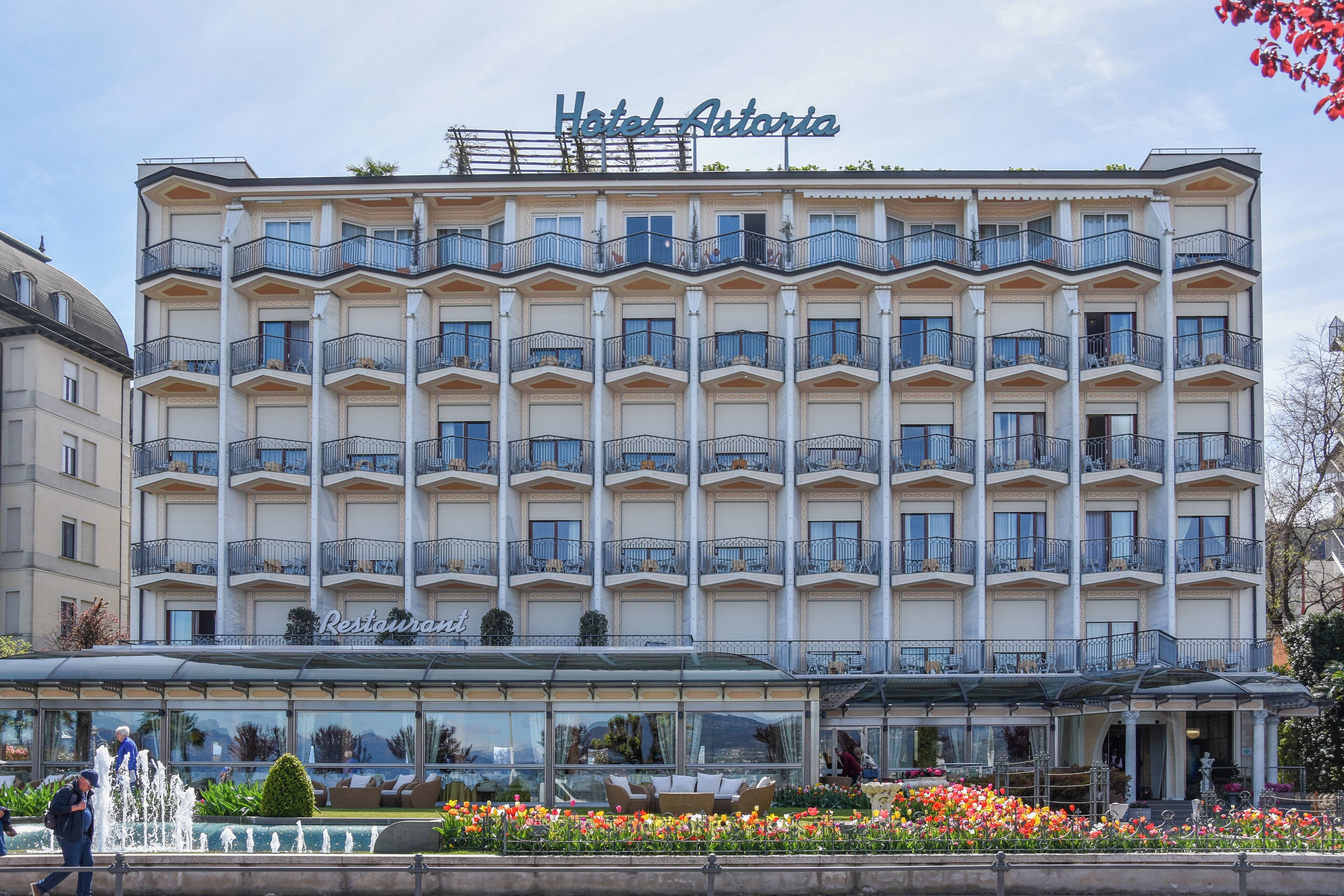 A multi-story hotel with balconies, a restaurant, and a fountain.