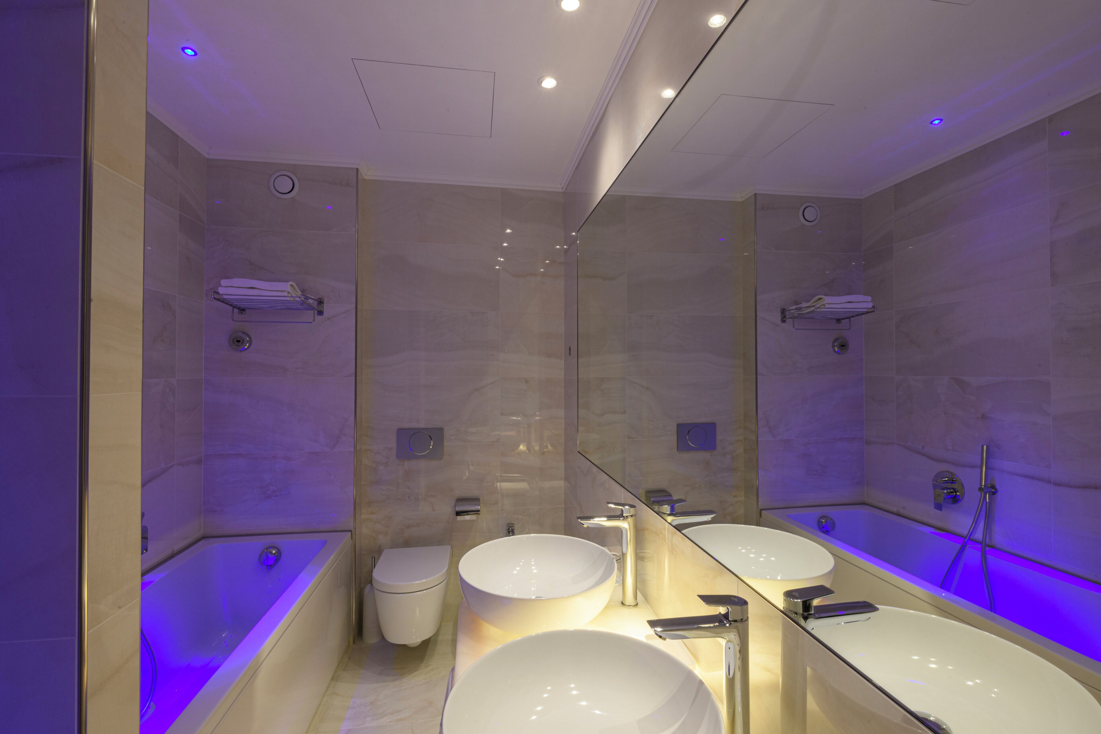 Un baño moderno con un espejo grande, dos lavamanos, una bañera y un inodoro.
