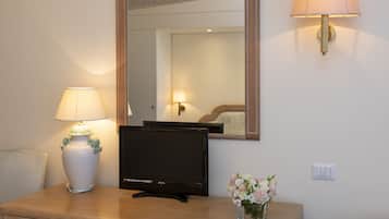 Quarto de hotel com televisão de tela plana, um vaso com flores e um espelho na parede.
