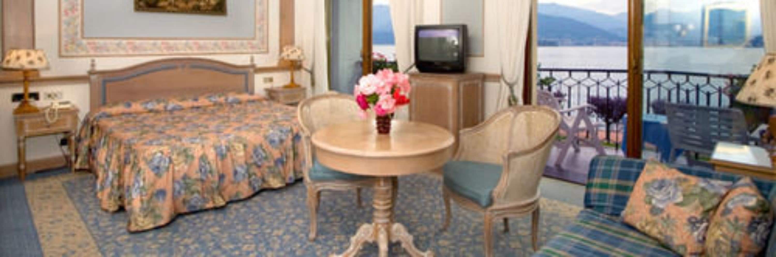 A hotel room with a bed, a table with a vase of flowers, a chair, a sofa, and a view of a body of water through a balcony.