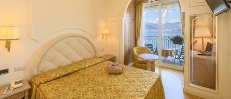 Una camera d'albergo con un letto, comodino, lampada, televisore e un balcone con tavolo e sedia.