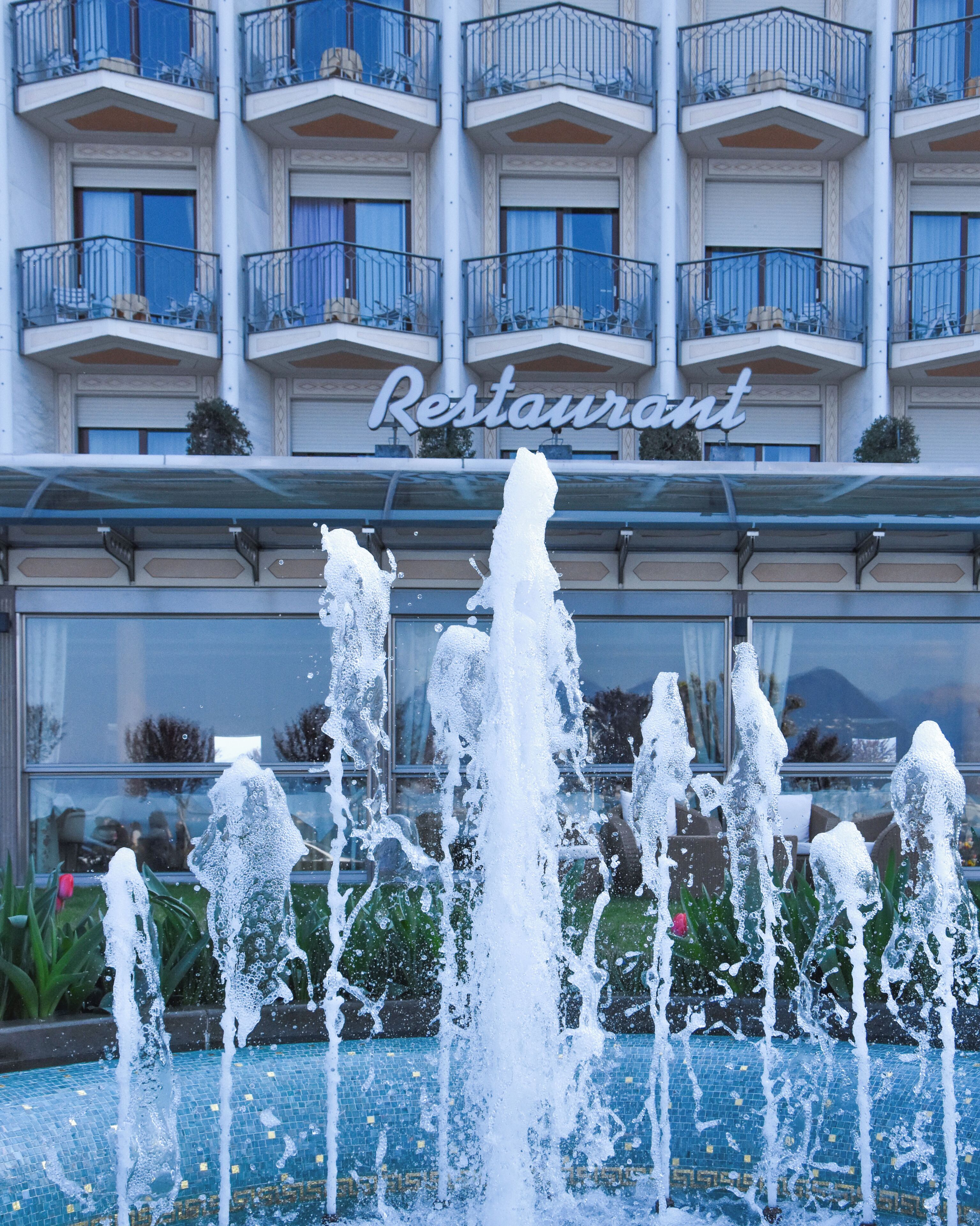 Un hotel con una fuente en primer plano, balcones con sillas y un cartel que dice "Restaurant".