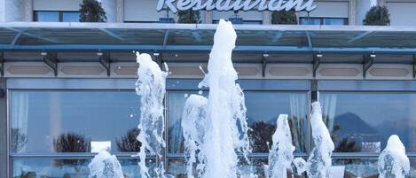 Un hotel con una fuente en primer plano, balcones con sillas y un cartel que dice "Restaurant".