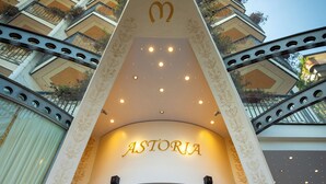La entrada de un hotel con el nombre 'ASTORIA' iluminado en la pared.