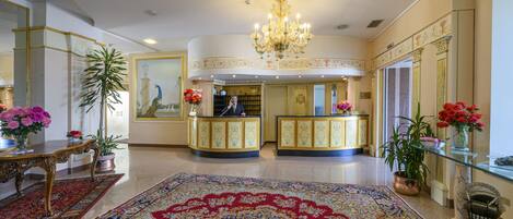A grand lobby with ornate decor, a reception desk, and a large chandelier.