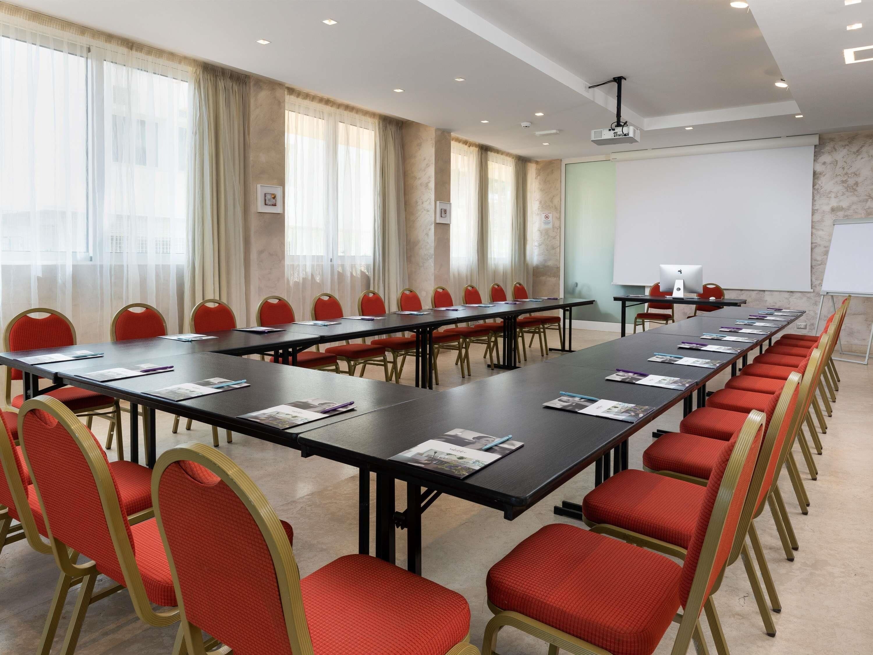A conference room with long tables, red chairs, a whiteboard, and a projector.