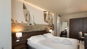 Et hotelværelse med en stor seng, et natbord med lampe, et garderobeskab og et billede af sejlbåde på væggen.