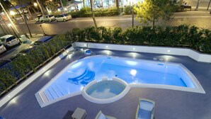En swimmingpool med et boblebad, liggestole og en flisebelagt terrasse.