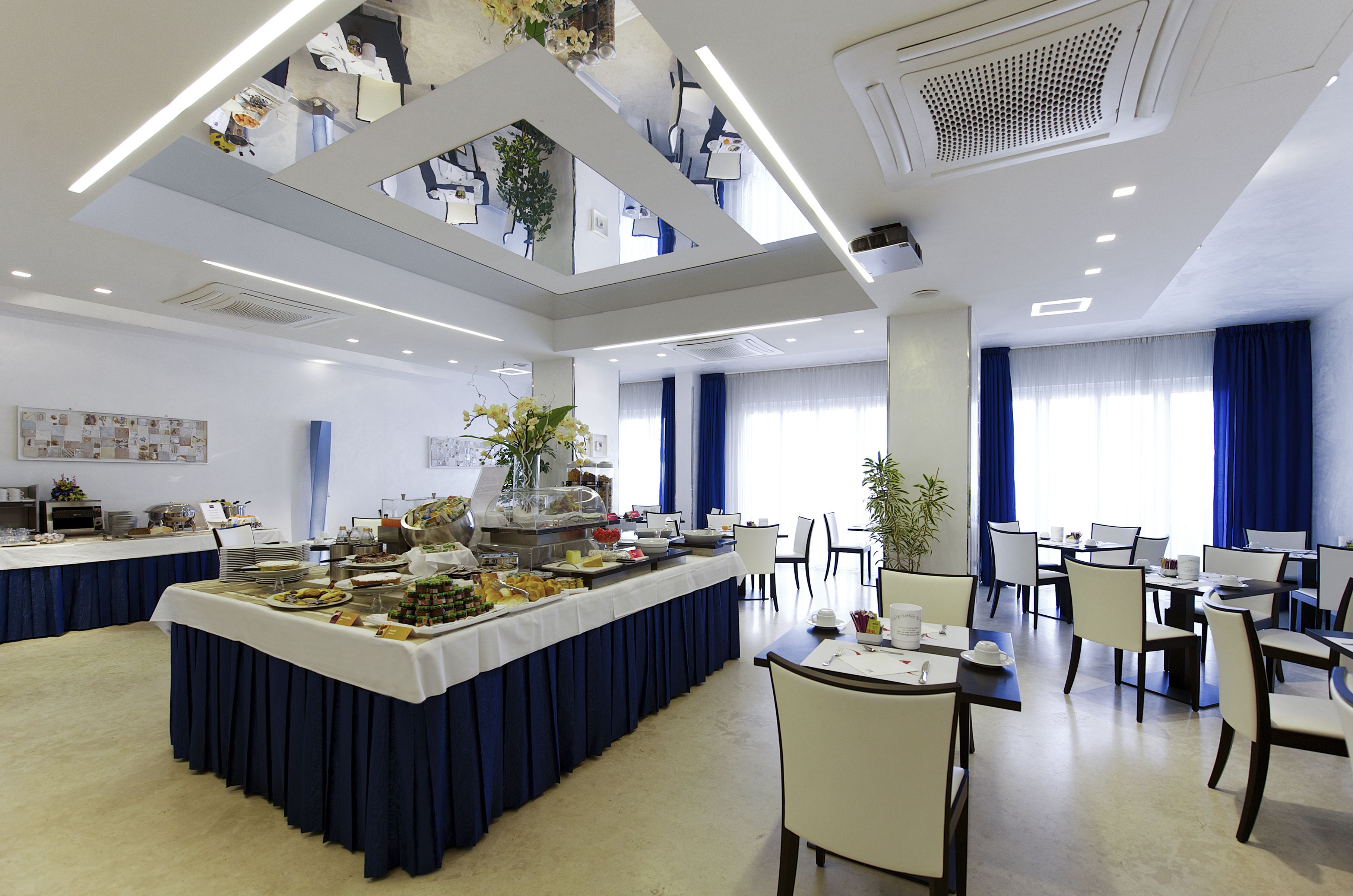 Un espace de restauration moderne dans un hôtel, avec un buffet, plusieurs tables et chaises.