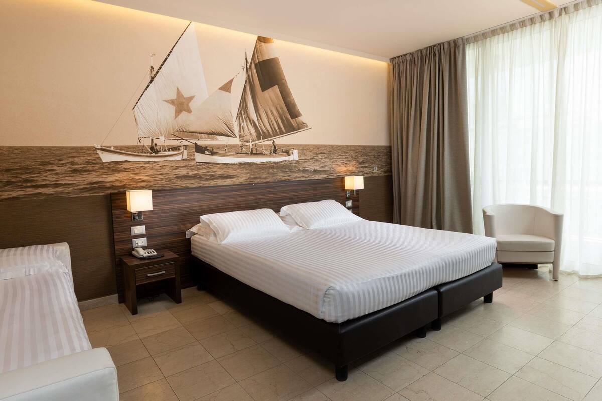 A hotel room with a large bed, two bedside tables with lamps, a chair, and a mural of a sailboat on the wall.