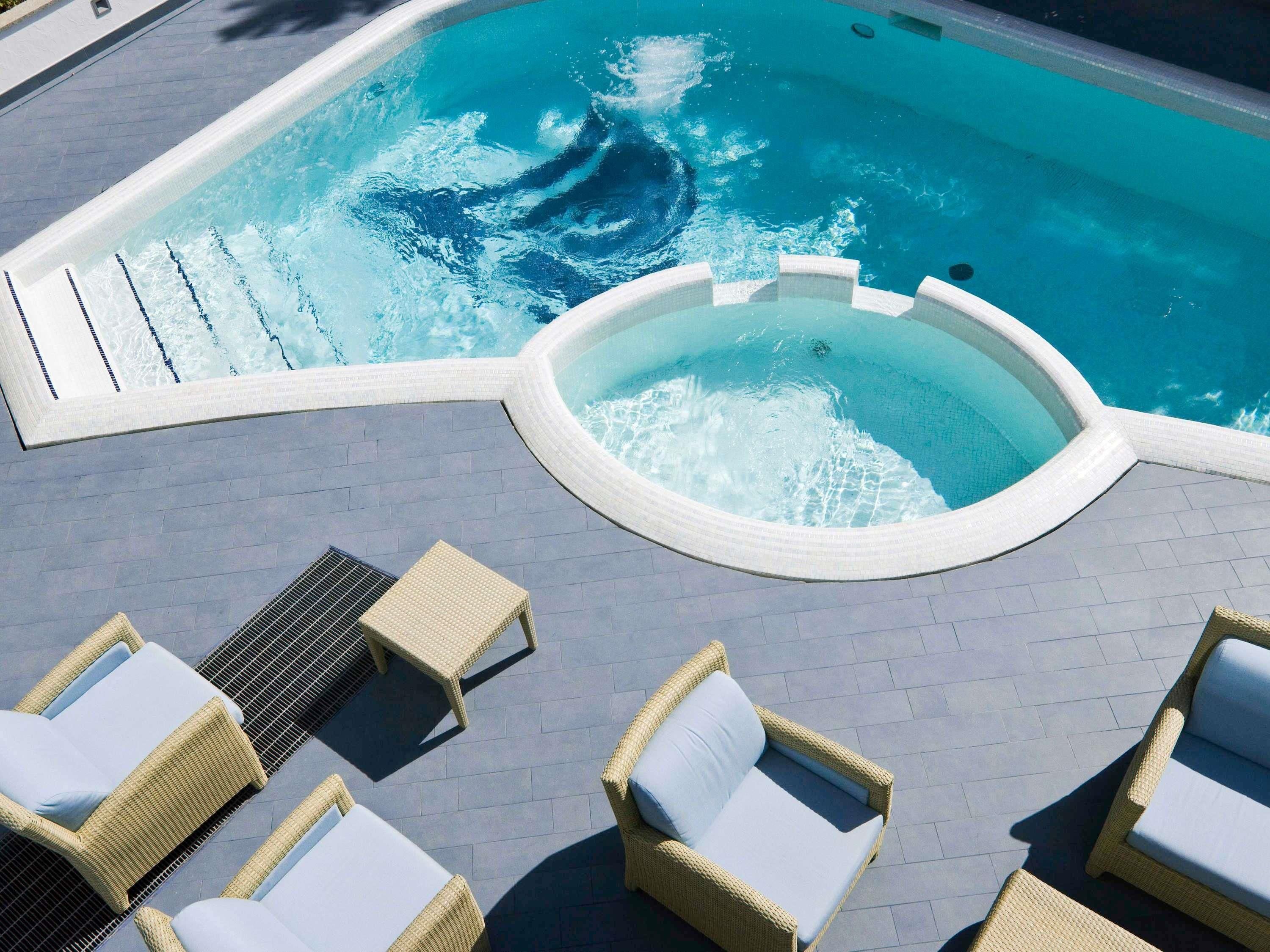 Una piscina con hidromasaje, rodeada de sillas de descanso y una terraza con baldosas.