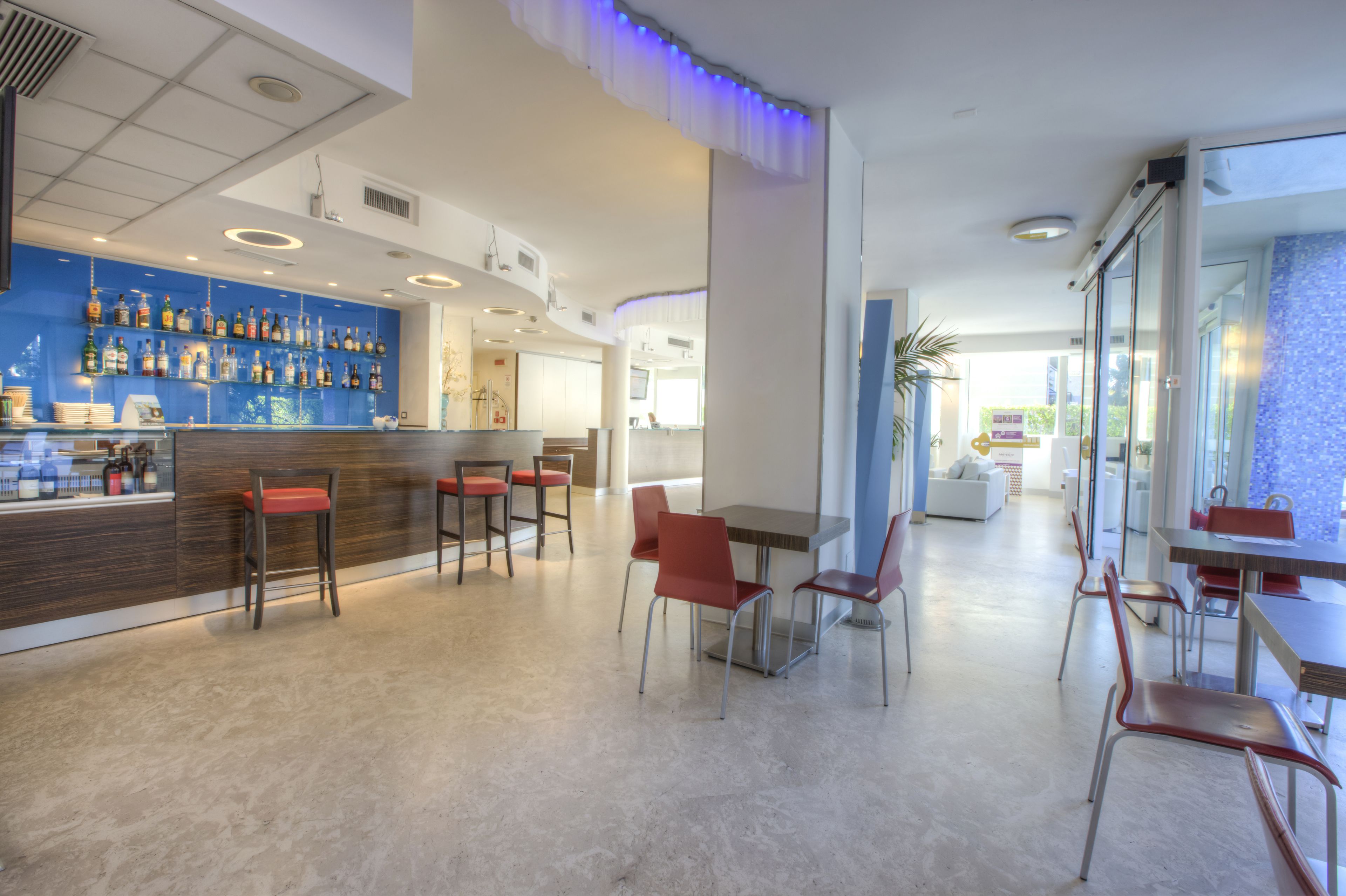 Un moderno hall de hotel con zona de bar, arreglos de asientos y vistas al exterior.