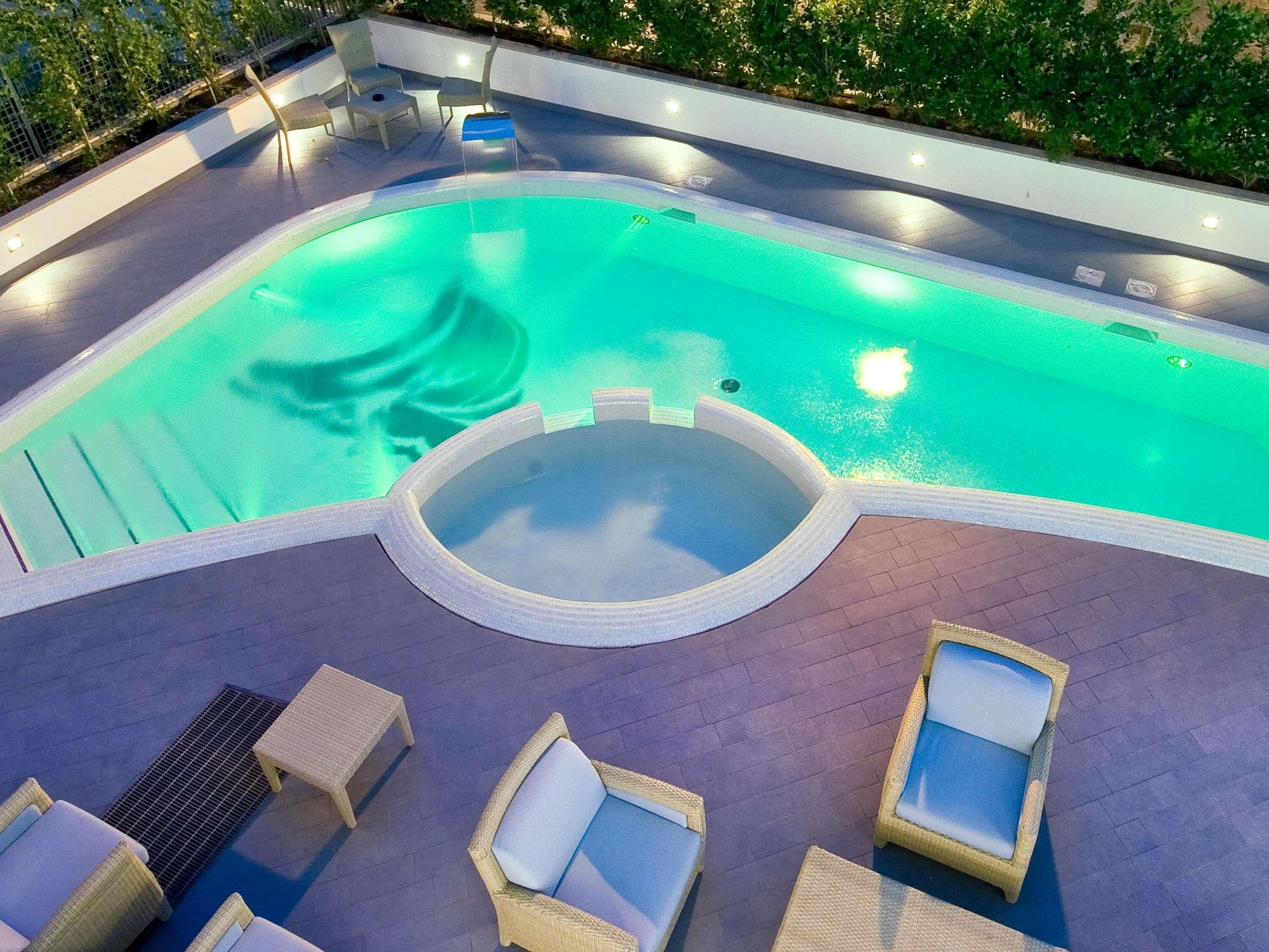 A swimming pool with a hot tub, lounge chairs, and a sun deck.