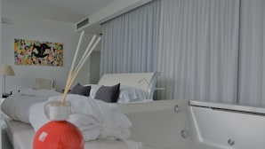 Een moderne hotelkamer met een bed, een nachtkastje met een rode vaas, en een kleurrijk abstract schilderij aan de muur.