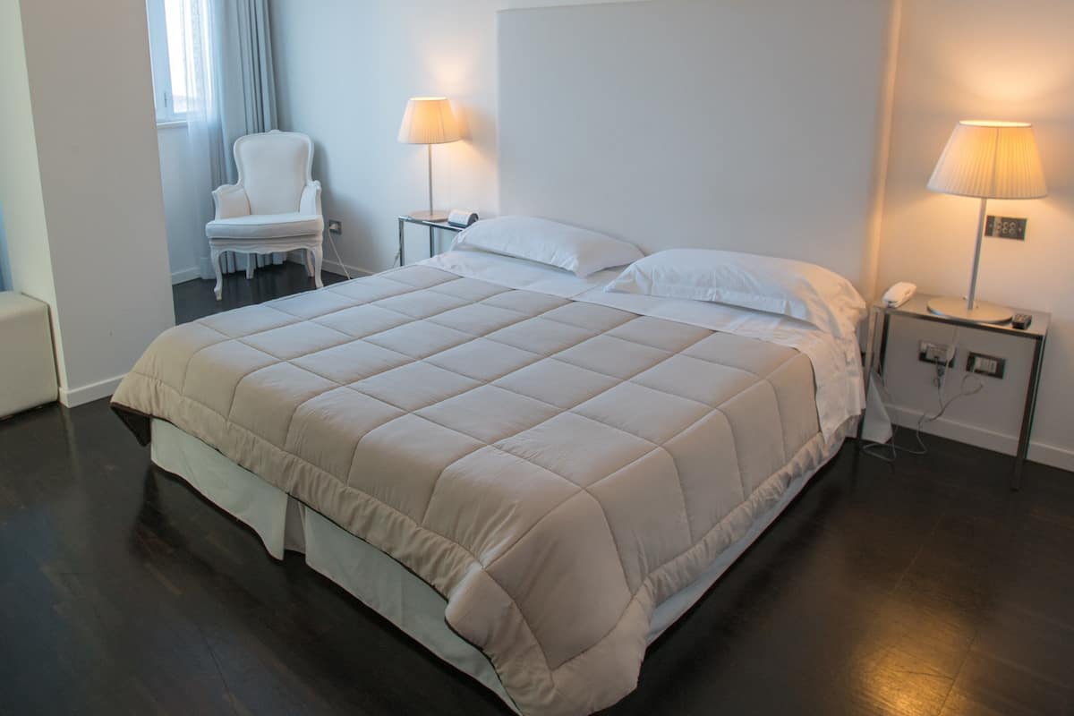 A hotel room with a large bed, two bedside tables with lamps, a chair, and a window with curtains.