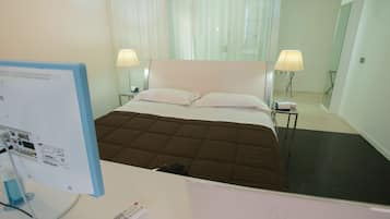 A hotel room with a bed, two bedside lamps, a desk with a computer monitor, and a remote control.