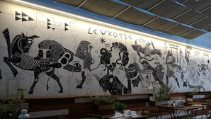 Een restaurant met een muurschildering van oude Egyptische en Azteekse ontwerpen, houten tafels en banken, en potplanten.