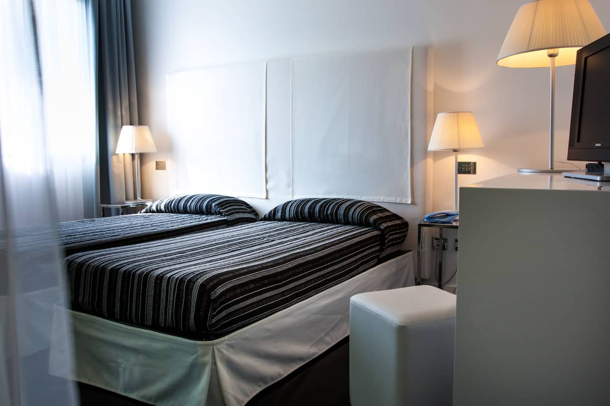 A hotel room with two beds, a desk, a chair, and two lamps.