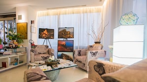 Een woonkamer met twee banken, een salontafel en een boekenkast. Er hangen drie ingelijste foto's aan de muur, staat een potplant en een decoratieve vaas.