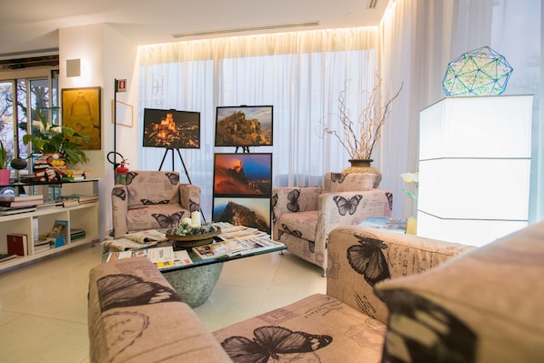 Una sala de estar con dos sofás, una mesa de centro y una estantería. Se observan tres cuadros enmarcados en la pared, una planta en maceta y un jarrón decorativo.