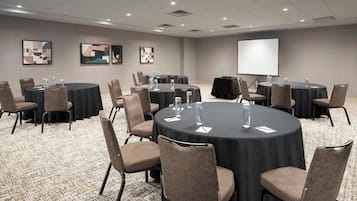 Una sala de conferencias con varias mesas, sillas y una pantalla para proyector.