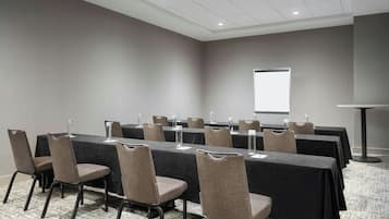 Une salle de conférence équipée de longues tables, de chaises, d’un écran de projection et d’un pupitre.