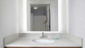 Een badkamer met een wit wastafel, een spiegel en een douche in de achtergrond.