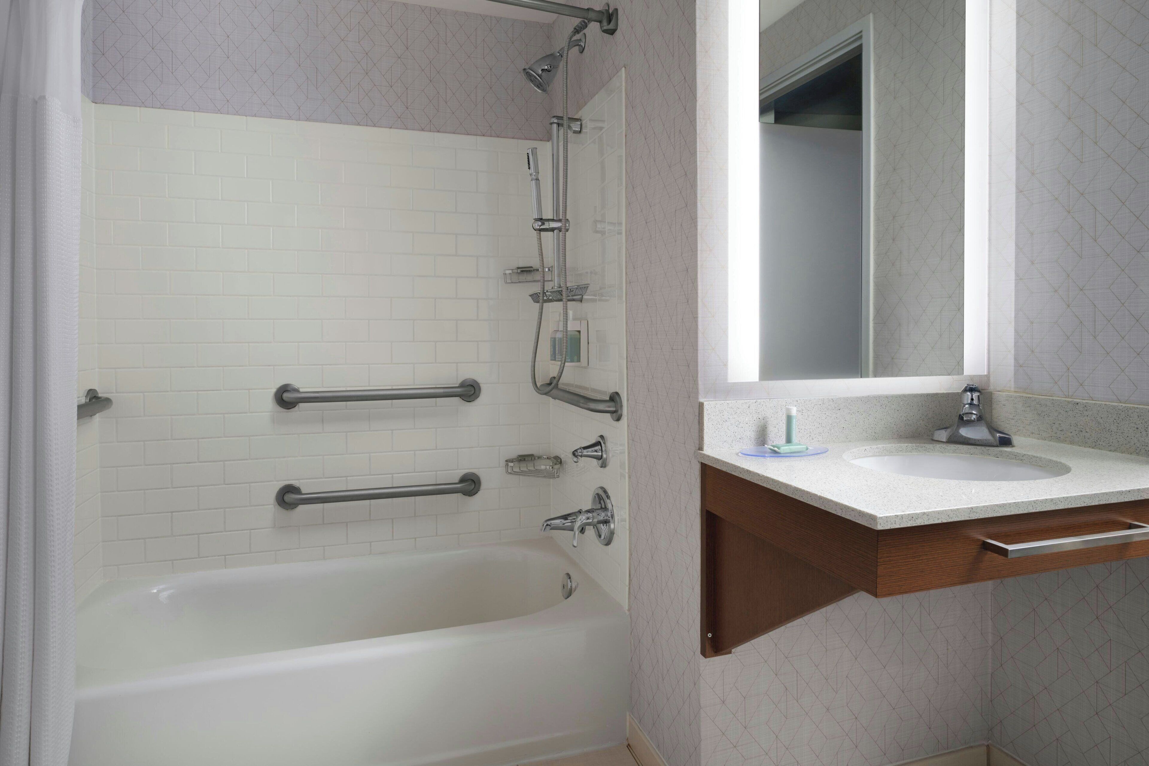 Een badkamer met een witte badkuip, een wastafel met een spiegel erboven en een douchekop.