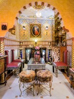 An ornate room with a central table, two red cushioned chairs, and a decorative vase.