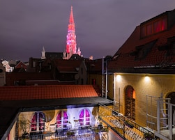 Een gebouw met een rood pannendak, een balkon met versierde hekwerk en een uitzicht op een verre toren met rode verlichting.